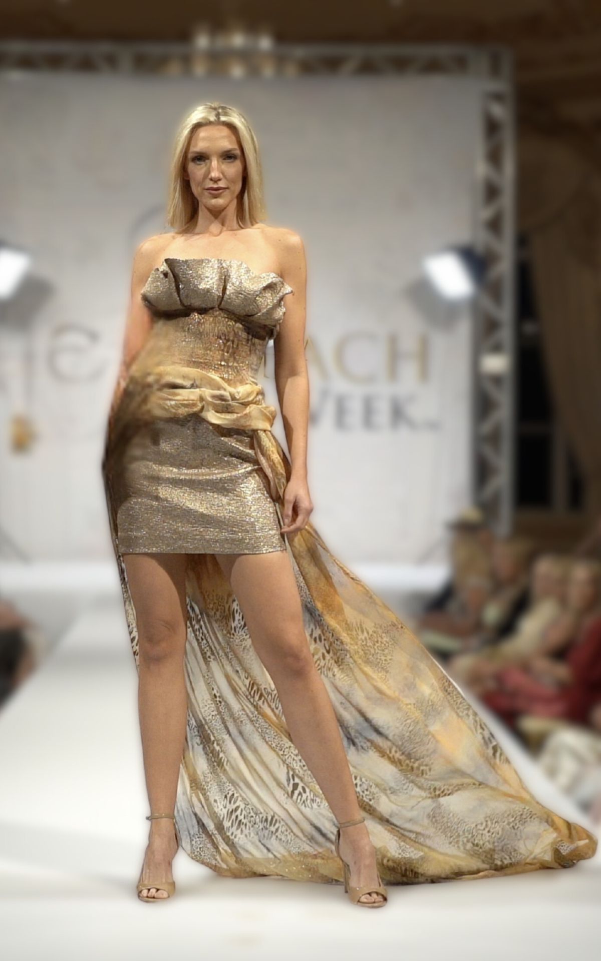 Model walks runway in Birgit C Muller gold lame and Cavalli fabric bustier skirt set with dramatic train at Palm Beach Fashion Week show