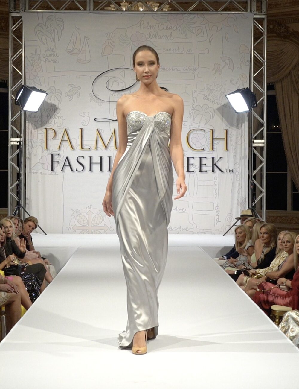 Model on runway wearing silver silk satin gown with beaded top at Palm Beach Fashion Week fashion show
