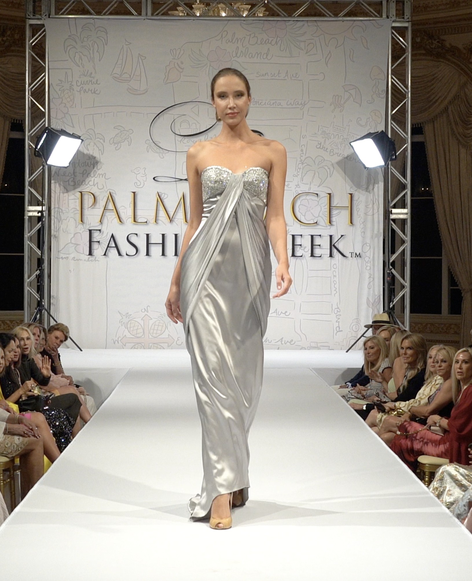 Model on runway wearing silver silk satin gown with beaded top at Palm Beach Fashion Week fashion show